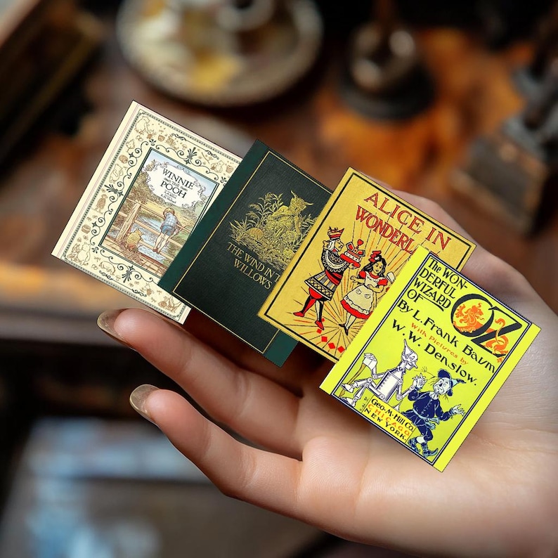 May include: A hand holding four miniature books with colorful covers. Titles include "Winnie the Pooh", "The Wind in the Willows", "Alice in Wonderland", and "The Wonderful Wizard of Oz". The books have detailed illustrations and text.