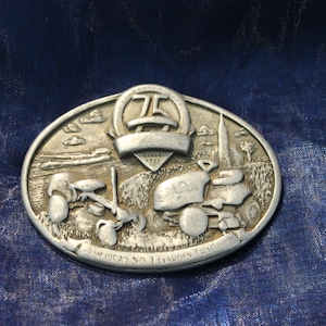 May include: Silver oval-shaped belt buckle with a raised design of two lawn tractors and the text "America's No. 1 Garden Tractor" and a banner with the number "75" and the text "Years 1937-2012".