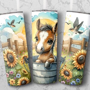 May include: Three white insulated tumblers with a watercolor design. Each tumbler features a brown and white foal in a metal bucket, sunflowers, a wooden fence, and birds against a blue sky and yellow sun.