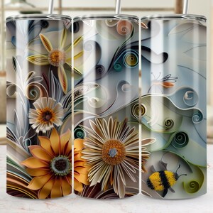 Op de afbeelding: Drie roestvrijstalen bekers met een kleurrijk papierkunstontwerp. Het ontwerp bevat een verscheidenheid aan bloemen, bladeren en swirls in tinten blauw, groen, geel en bruin. De bekers zijn perfect voor het vasthouden van warme of koude dranken.