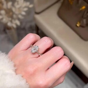 May include: A gold ring with an oval-cut diamond centre stone. The ring features a delicate band with smaller accent stones. The ring is worn on a finger, showcasing its elegant design and sparkle.