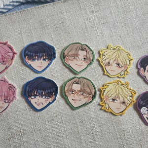 May include: A collection of ten die-cut stickers featuring illustrated anime-style character heads with various hair colors including pink, dark blue, light brown, blonde, and black, displaying diverse facial expressions and eye colors.