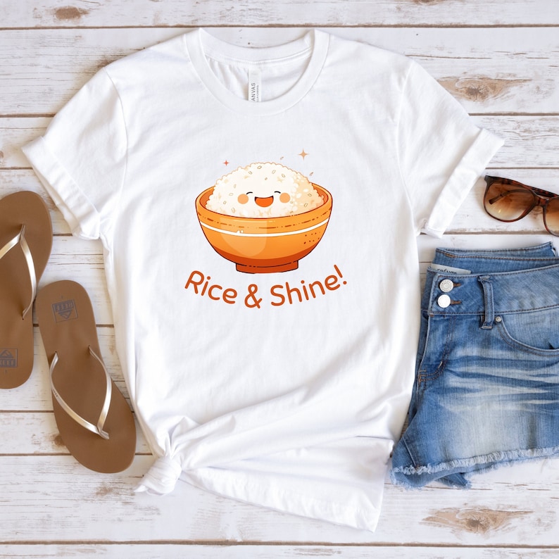 May include: White t-shirt featuring a cartoon bowl of rice with a smiling face. The bowl is orange, and the text "Rice & Shine!" is below the bowl. The shirt is paired with denim shorts and sandals.