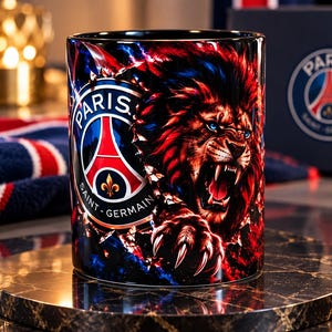 Könnte beinhalten: Ein zylindrischer Keramikbecher mit einer lebendigen Grafik eines brüllenden Löwen mit roter und blauer Mähne, platziert neben dem Logo des Fußballvereins Paris Saint-Germain. Das Design enthält scharfe, rot-blaue Splitterglaseffekte.