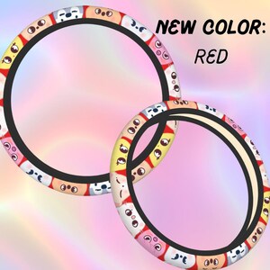K&ouml;nnte beinhalten: Zwei kreisf&ouml;rmige Lenkradbez&uuml;ge mit einem sich wiederholenden Muster aus bunten Cartoon-Gesichtern mit verschiedenen Ausdr&uuml;cken. Der Text NEW COLOR: RED ist rechts in Schwarz aufgedruckt. Die Bez&uuml;ge haben einen schwarzen Innenrand.