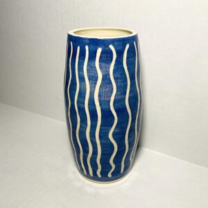 May include: A blue ceramic vase with white wavy lines. The vase is cylindrical and has a smooth, glossy finish.