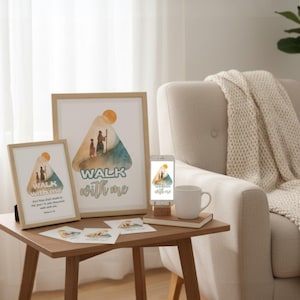 May include: Framed art prints and a smartphone display a watercolor design with the text "Walk With Me." The artwork features a family silhouette and a sun. A white mug and small cards are on a wooden table near a cream-colored armchair.