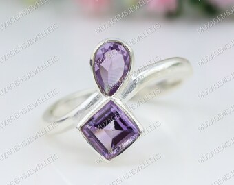 May include: A silver ring with two amethyst gemstones. The larger gemstone is square shaped and the smaller gemstone is pear shaped.