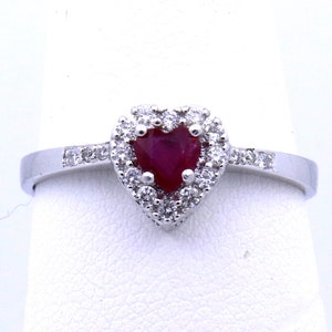 May include: A heart-shaped ruby ring with a halo of small diamonds set in white gold.