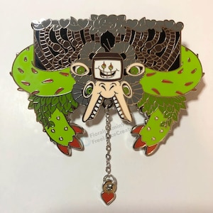 May include: An enamel pin depicting a fantastical creature with a TV screen face, green cactus-like wings, and a chain with a heart charm. The pin is in shades of green, grey, black, and red, with intricate detailing.