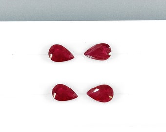 May include: Four pear-shaped red gemstones on a white surface.
