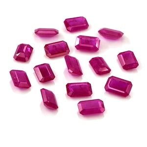 Puede incluir: Una colección de quince piedras preciosas facetadas sueltas en un vibrante tono rosa magenta. Cada piedra presenta un corte esmeralda rectangular con bordes limpios y una superficie pulida, dispuestas en un grupo sobre un fondo blanco.