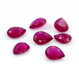 Könnte beinhalten: Eine Ansammlung von sechs losen, birnenförmigen Rubinen mit einem leuchtenden, tiefen pink-roten Farbton. Jeder Edelstein weist eine facettierte Oberfläche auf, die das Licht reflektiert und ein brillantes, poliertes Finish zeigt.