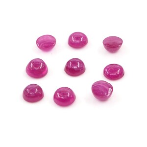 May include: Eight small, round, cabochon-cut gemstones in a vibrant magenta-pink color. Each stone features a smooth, domed top surface and a flat base, displaying a consistent polished finish and a translucent quality across the entire collection.