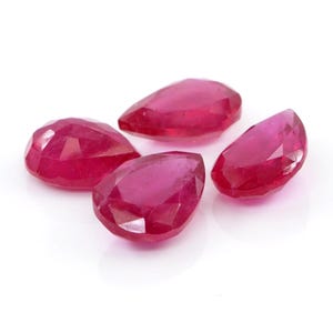 May include: Four loose, pear-shaped rubies with a vibrant, deep red colour and faceted surfaces. Each gemstone displays a polished finish with multiple geometric cuts that reflect light, showcasing the translucent quality of the red stones.