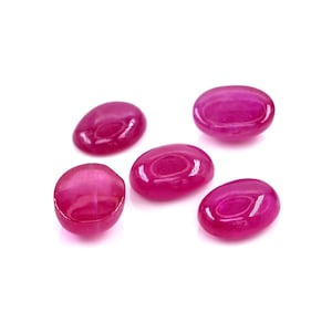 Op de afbeelding: Vijf losse, ovaalvormige robijnen met een gladde, gepolijste cabochonafwerking. Elke edelsteen vertoont een levendige, diep magenta-rode kleur met een glanzend oppervlak dat licht reflecteert en een doorschijnende kwaliteit laat zien.