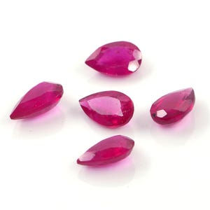 May include: Five loose, pear-shaped gemstones with a vibrant, deep magenta-red color. Each stone features a faceted surface that reflects light, creating a brilliant appearance. The gems are arranged in a cluster against a plain white background.