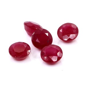 Puede incluir: Una colección de cinco rubíes sueltos, de corte redondo, con un color rojo intenso y superficies facetadas. Cada piedra preciosa muestra una calidad brillante y reflectante con múltiples facetas triangulares en la parte superior.