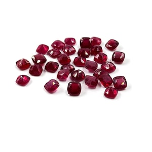 May include: A loose pile of 20 small, red, square-shaped gemstones. The gemstones are faceted and have a shiny, polished finish.