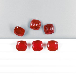 May include: Six red gemstone cabochons, some arranged in a row and some in a semi-circle.