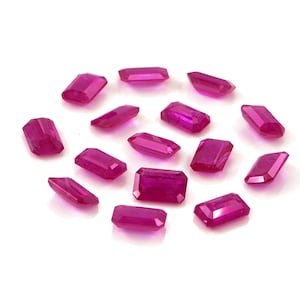 Puede incluir: Una colección de catorce piedras preciosas sueltas de color rosa rojizo vibrante, cada una tallada en forma de esmeralda rectangular con superficies facetadas que reflejan la luz, dispuestas en un grupo disperso sobre un fondo blanco.