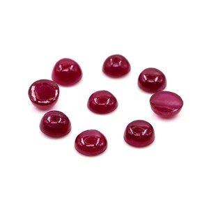 Könnte beinhalten: Eine Ansammlung von neun kleinen, runden, im Cabochon-Schliff bearbeiteten Rubinen mit tiefroter Farbe und einer glatten, polierten Oberfläche. Jeder Edelstein weist eine gewölbte Oberseite und eine flache Unterseite auf, mit leuchtendem Farbton.