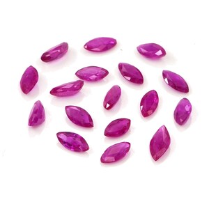 Puede incluir: Un conjunto de quince piedras preciosas sueltas con talla marquesa en un tono magenta rosado intenso y vibrante. Cada piedra presenta una superficie facetada que refleja la luz, mostrando una forma ovalada alargada y puntiaguda.