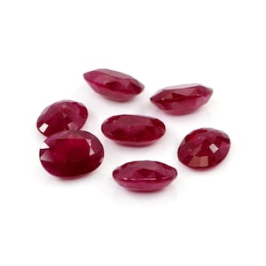 Puede incluir: Un conjunto de seis rubíes sueltos, tallados en forma ovalada, con un color rojo intenso y superficies facetadas. Cada piedra preciosa muestra un acabado pulido y una forma simétrica, dispuestas en grupo sobre un fondo blanco liso.