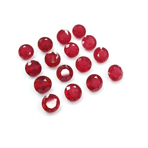 Puede incluir: Una colección de 17 piedras preciosas redondas de color rojo. Las piedras preciosas están dispuestas en un patrón escalonado sobre un fondo blanco.