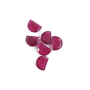 May include: Six ruby red half-round gemstones, each with a faceted surface, arranged in a cluster on a white background.