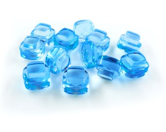 Puede incluir: Un grupo de cristales cuadrados facetados de color azul claro dispersos sobre un fondo blanco.