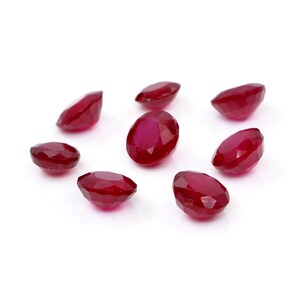 May include: A collection of seven loose, faceted rubies with a deep red color and an oval shape. Each gemstone features a polished surface with multiple triangular facets that reflect light, showcasing the vibrant, saturated red hue of the stones.