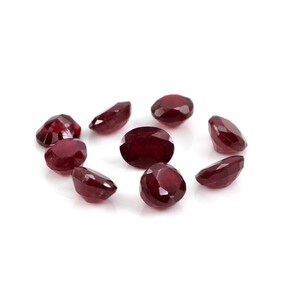 Puede incluir: Colección de nueve rubíes facetados, de formas ovaladas y de lágrima, dispuestos en círculo. Las piedras preciosas son de un color rojo intenso y rico, con variaciones de tamaño y talla. Fondo blanco. Ideal para joyería.