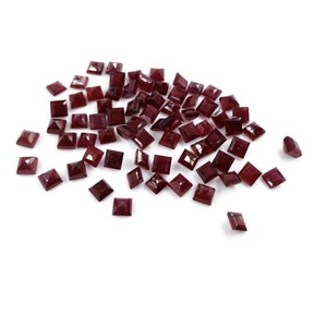 May include: A pile of loose, dark red square-shaped gemstones.