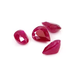 Puede incluir: Cuatro rubíes facetados sueltos de un color rojo vibrante. Cada piedra preciosa presenta una forma de pera distintiva con múltiples facetas triangulares y en forma de cometa que reflejan la luz, creando una apariencia brillante en la superficie.
