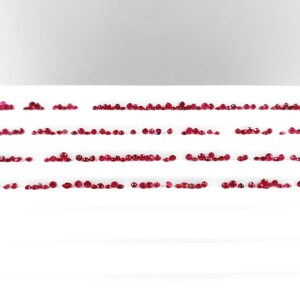 Könnte beinhalten: Ein weißes Tablett mit Reihen kleiner, roter Rubin-Edelsteine.