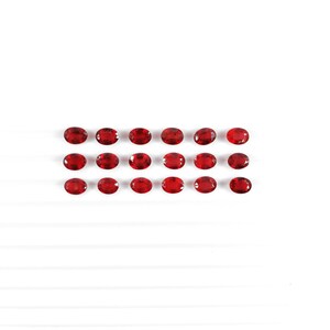May include: Twenty red oval-shaped gemstones arranged in two rows on a white background.