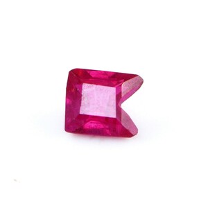 May include: A vibrant, deep pinkish-red gemstone with a unique, asymmetrical geometric cut. The stone features a square-like base that tapers into a sharp, pointed triangular edge on one side, showcasing multiple faceted surfaces that reflect light.