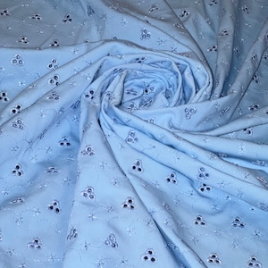 May include: Light blue cotton fabric with a delicate eyelet pattern. The fabric is folded and draped, showcasing the intricate design.