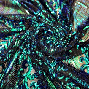 May include: Close-up of a black fabric covered in teal and blue sequins. The sequins are arranged in a swirling pattern, creating a shimmering effect. The fabric has a mesh backing.