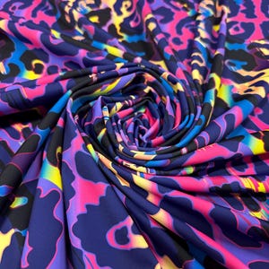 Könnte beinhalten: Lebendiger Stoff mit farbenfrohem Leopardenmuster. Das Design zeigt einen dunkelblauen Hintergrund mit leuchtend pinken, gelben und blauen Flecken. Der Stoff ist gerafft und gewirbelt, wodurch der Fluss des Musters zur Geltung kommt.
