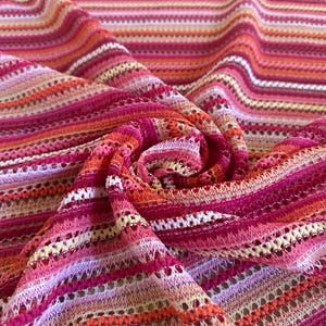 Könnte beinhalten: Nahaufnahme eines bunten Stoffes mit Streifenmuster. Der Stoff weist eine Mischung aus Rosa-, Orange- und Weißtönen auf und erzeugt ein ansprechendes Design. Das Material scheint leicht und möglicherweise gestrickt oder gehäkelt zu sein.