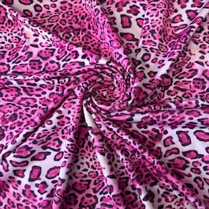 May include: Pink and white fabric with a leopard print pattern. The fabric is folded and draped, showing the texture and detail of the print.