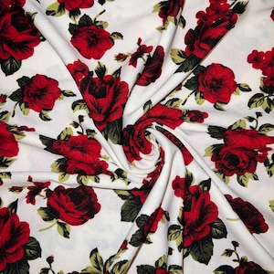 May include: White fabric with a red and green floral pattern. The fabric is a soft, lightweight material with a subtle texture. The flowers are a variety of sizes and shapes, and they are arranged in a random pattern.