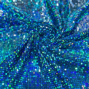 May include: Close-up of a shimmering fabric with a mosaic pattern. The fabric is a deep blue with iridescent squares that reflect shades of green and blue. The material is draped, creating folds and shadows.