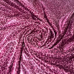 May include: Close-up of a fabric with a pink and magenta leopard print pattern. The fabric is gathered and folded, creating a swirling effect. The material has a shiny, metallic appearance.