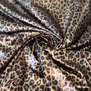 May include: Close-up of a brown and black leopard print fabric with a shiny, satin-like finish.