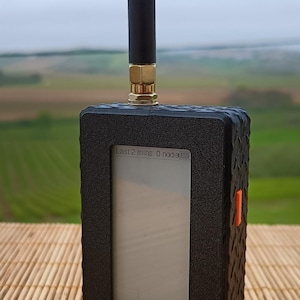 Peut inclure: Un appareil électronique rectangulaire noir avec un boîtier texturé à motif losange, une antenne noire verticale avec une base dorée et un écran rectangulaire central affichant le texte Last 2 mins: 0 nod, avec un bouton latéral orange.