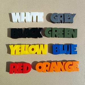 K&ouml;nnte beinhalten: Ein Satz von 10 Farbbl&ouml;cken, jeder mit einer anderen Farbe und dem Wort f&uuml;r diese Farbe in Gro&szlig;buchstaben geschrieben. Die Farben sind Wei&szlig;, Grau, Schwarz, Gr&uuml;n, Gelb, Blau, Rot und Orange.