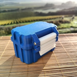 Könnte beinhalten: Eine kleine, blaue, Plastik-Aufbewahrungsbox mit einem weißen Verschluss. Die Box steht auf einer Bambusmatte.